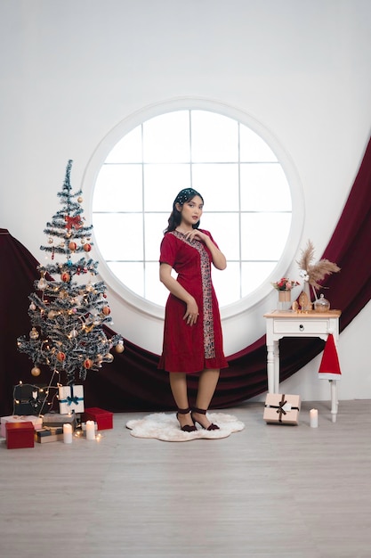 Portrait of a pretty young girl wearing a red gown smiling at the camera standing in decorated christmas living room indoors