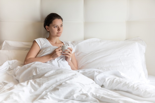 Портрет хорошенькая молодая девушка с кофе на кровати в первой половине дня