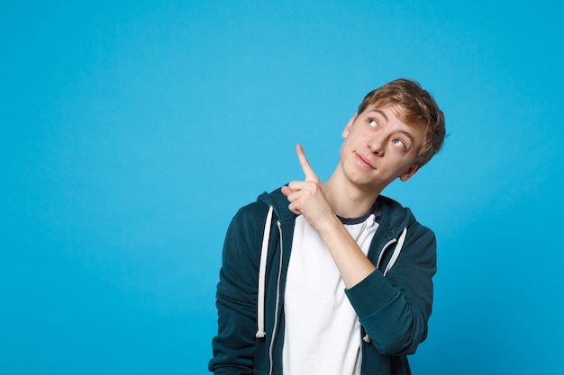 Portrait of pretty young man in casual clothes pointing index fingers aside and looking up isolated