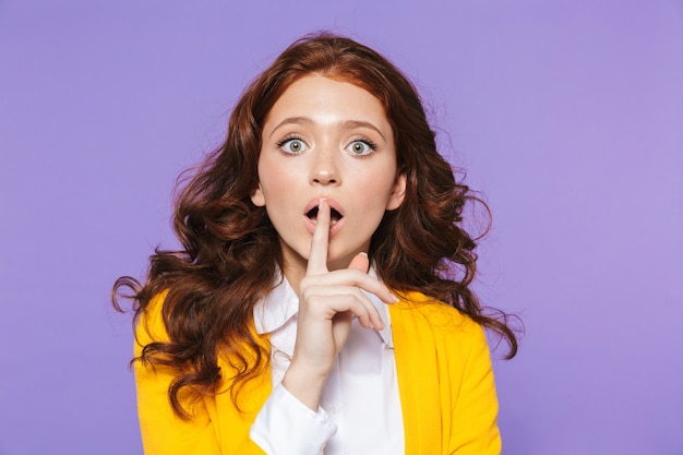 Portrait of a pretty young redheaded woman standing over violet, showing silence gesture