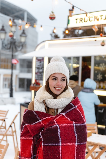 格子縞を着て冬の雪の中で屋外を歩く帽子とスカーフのかなり若い女性の肖像画。