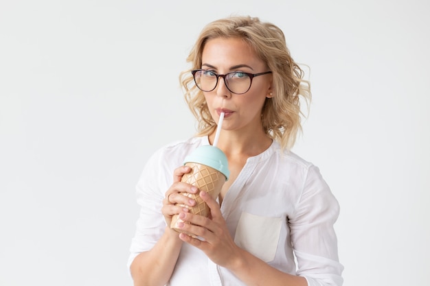 Portrait of pretty young woman is drinking smoothie over white wall