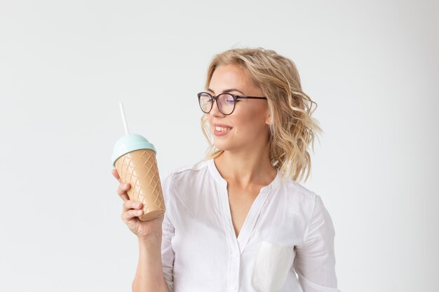 Portrait of pretty young woman is drinking smoothie over white wall