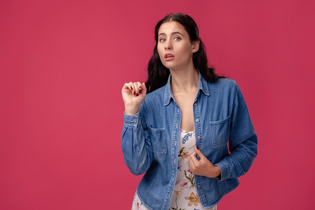 Portrait of a pretty young woman in a light dress and blue shirt standing on pink background in studio. People sincere emotions.