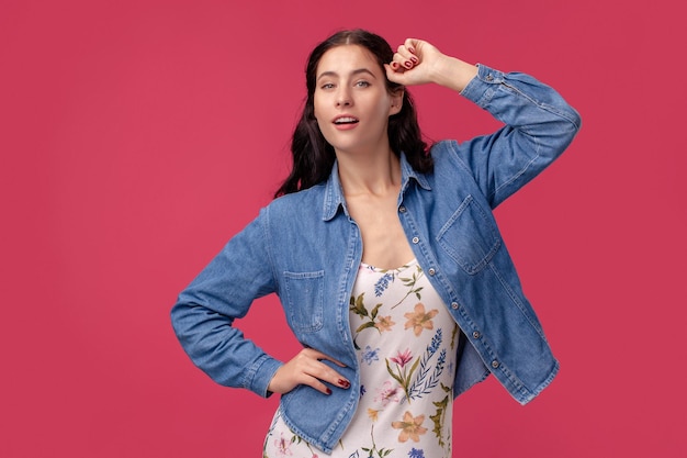 Portrait of a pretty young woman in a light dress and blue shirt standing on pink background in studio. People sincere emotions.