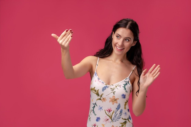 Portrait of a pretty young woman in a light dress standing on pink background in studio. People sincere emotions.