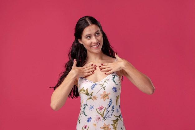 Portrait of a pretty young woman in a light dress standing on pink background in studio. People sincere emotions.