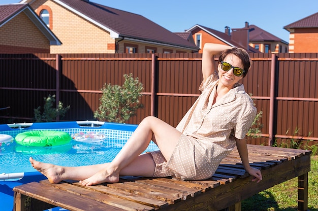 Portrait of pretty young woman in pajama sitting near inflatable swimming pool summer and country l