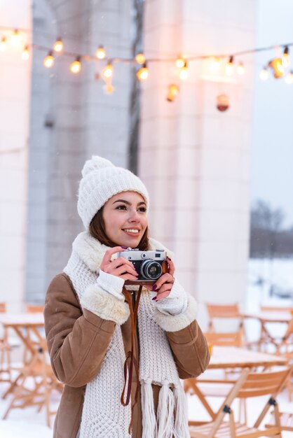 Foto ritratto di una bella giovane donna ritrattista turista in cappello e sciarpa passeggiate all'aperto in inverno neve tenendo la fotocamera.