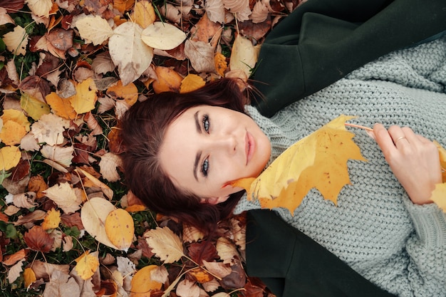 Portrait of pretty young woman of Slavic appearance in casual clothing in autumn, lying on autumn yellow leaves. Cute model walks in Park in golden fall against background of nature. Copy space