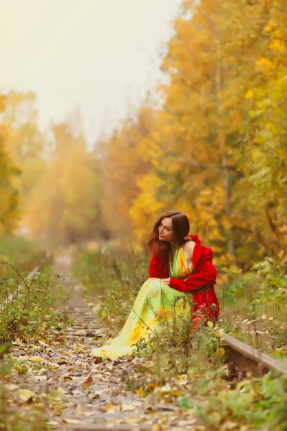 Photo portrait of pretty young woman of slavic appearance in yellow colored dress and red coat in autumn, walk in forest