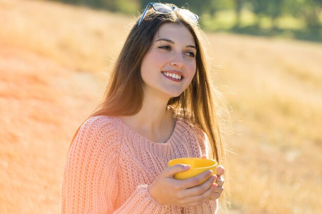 Portrait of pretty young woman in stylish knitted sweater standing on the golden autumn forest on sunny day