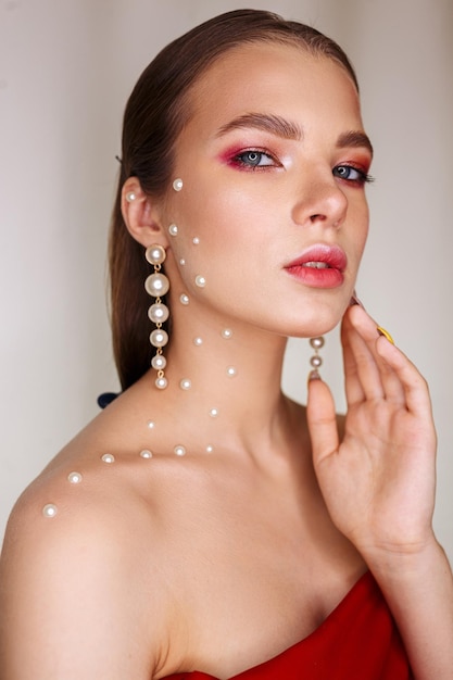 Portrait of pretty young woman with pearls touching face and looking at camera in studio