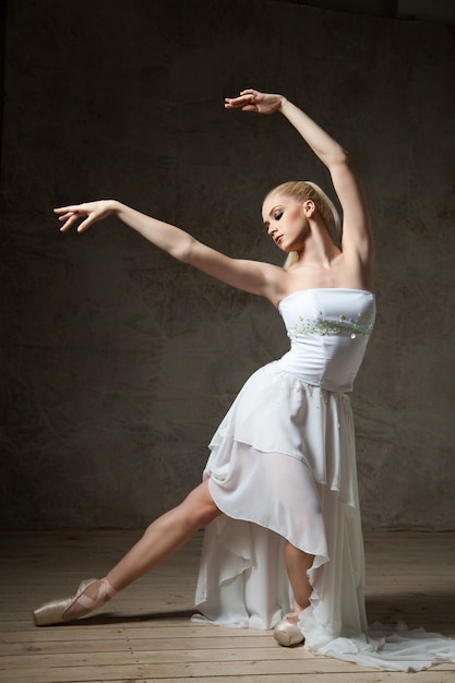 Foto ritratto di ballerina professionista in abito bianco che si esibisce in studio con le braccia alzate