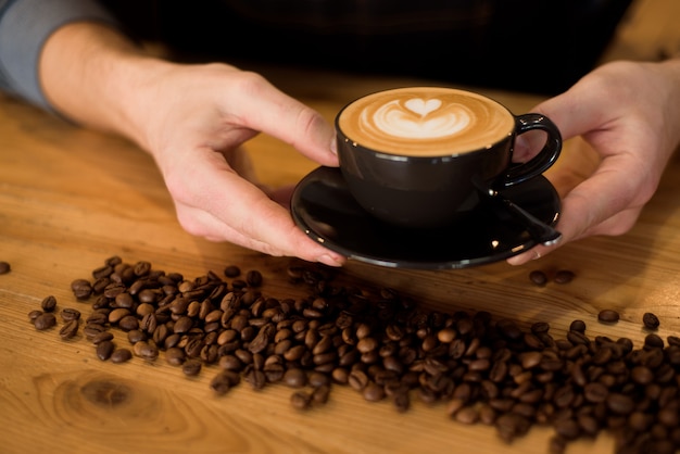 Portrait of professional barista man in apron holding cup of hot coffee at a cafe