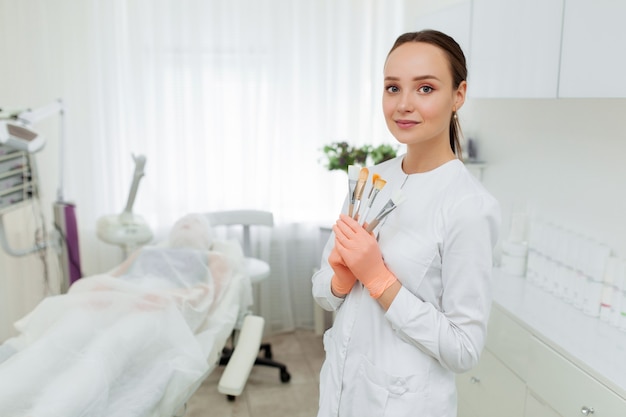 Portrait of a professional beautician with brushes in hands. Beautiful caucasian woman on a cosmetology procedure.