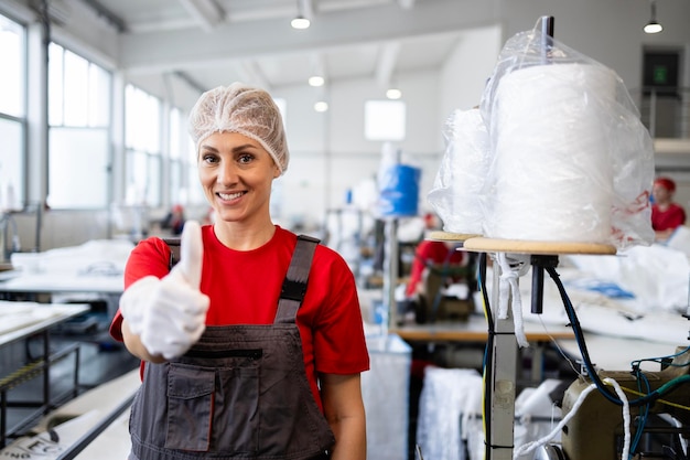 Portrait of professional female tailor standing by sewing machine inside textile factory