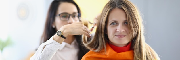 Portrait of professional hairdresser cutting hair with special instrument woman covered with