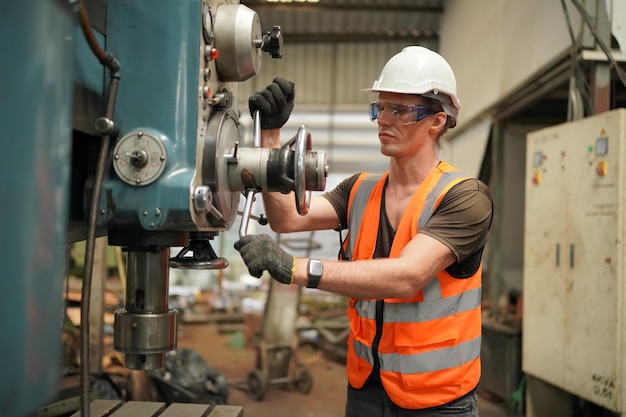 Portrait of Professional Heavy Industry Engineer / Worker Wearing Safety Uniform, Goggles and Hard Hat. In the Background Unfocused Large Industrial Factory