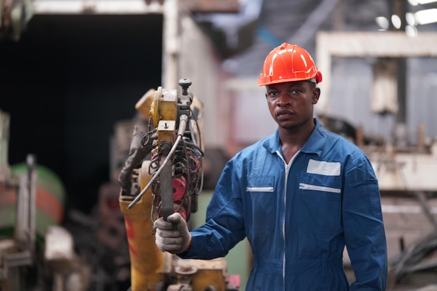 Portrait of Professional Heavy Industry Engineer / Worker Wearing Safety Uniform, Goggles and Hard Hat. In the Background Unfocused Large Industrial Factory