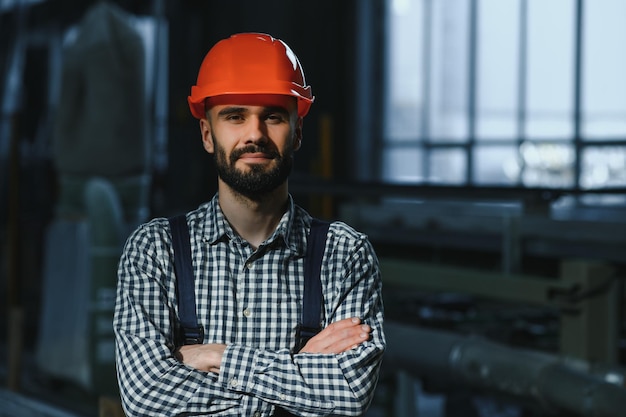 Portrait of professional heavy industry engineer worker wearing\
safety uniform hard hat smiling in the background unfocused large\
industrial factory