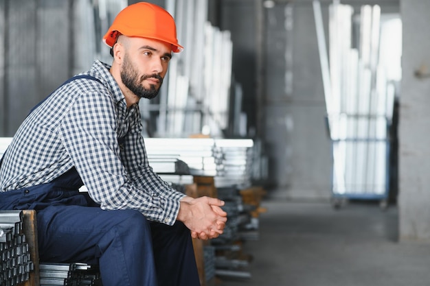 Portrait of Professional Heavy Industry Engineer Worker Wearing Safety Uniform Hard Hat Smiling In the Background Unfocused Large Industrial Factory