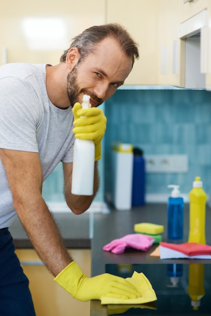 Ritratto di un professionista delle pulizie maschio che indossa guanti che guarda la macchina fotografica e usa un detergente spray