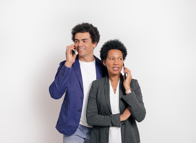 Portrait of professional partners discussing over smart phones while standing on white background