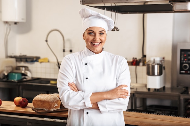 Portrait of professional woman chef wearing white uniform, posing in kitchen at the restaurant