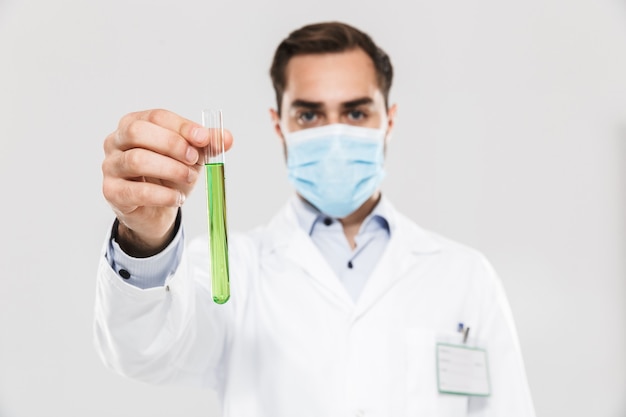 Portrait of professional young medical doctor working in clinic laboratory and holding test tube isolated over white wall