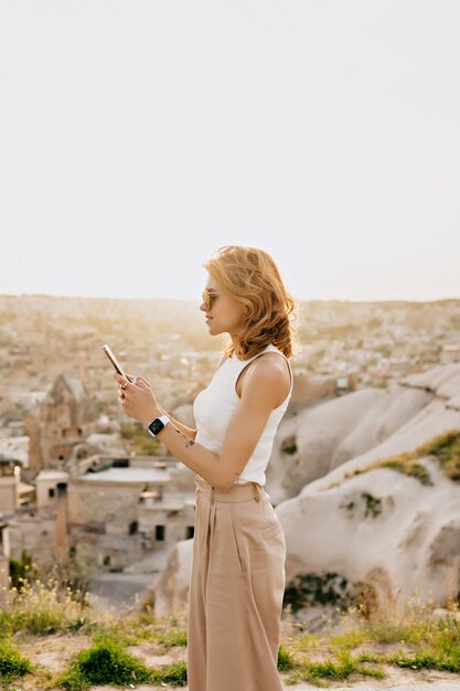 女性観光客のプロフィールの肖像画は山の風景にスマートフォンをスクロールしています