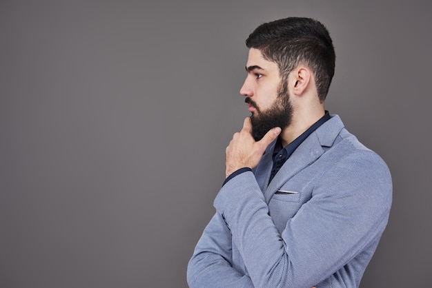 Photo portrait in profile of freelancer man with beard in jacket standing against gray backdrop.