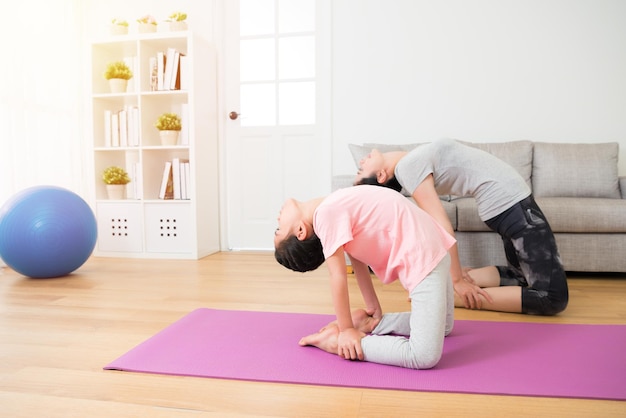 portrait of profile slim beautiful daughter and beauty mother doing same yoga sporting action stretch body with legs and hands at fitness center club room.