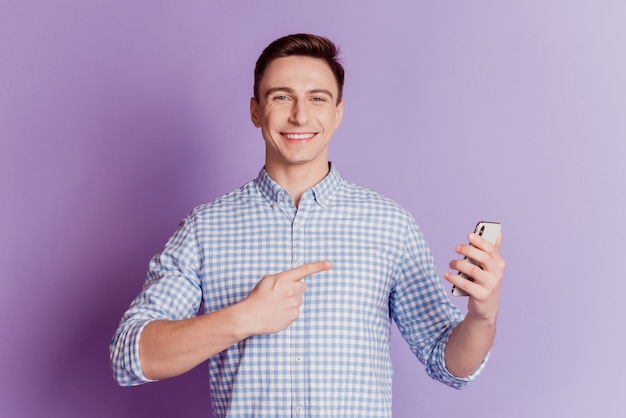 Portrait of promoter guy hold smartphone direct forefinger on purple background