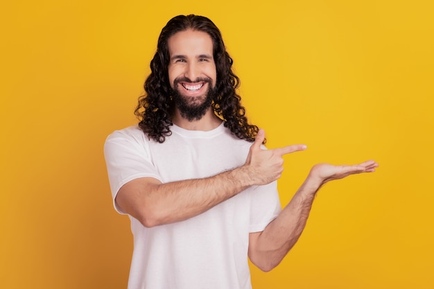 Portrait of promoter man direct forefinger hand hold blank space shiny smile on yellow background