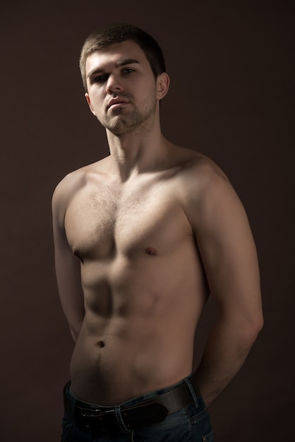 Photo portrait of a proud confident young male athlete with a beautiful figure and press cubes against a dark wall