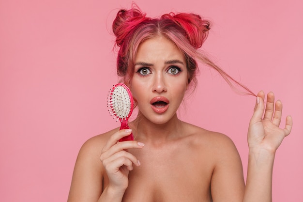Portrait of puzzled shirtless young woman touching her hair and holding brush