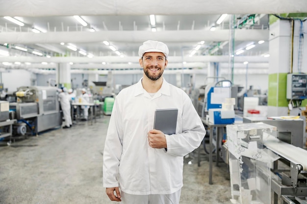 Portrait of a quality control worker at meat factory standing with tablet and smiling at the camera