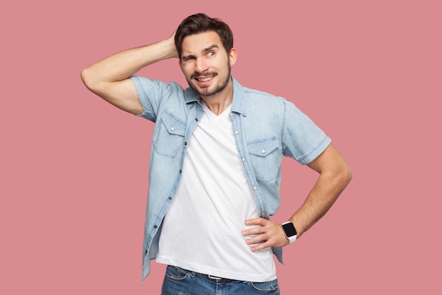 Portrait of query handsome bearded young man in blue casual style shirt standing and looking away and thinking what to do. indoor studio shot, isolated on pink background.