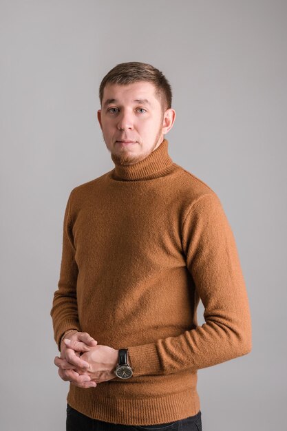 Portrait of a red-bearded man on a gray background. A young adult guy in a red sweater poses looking at the camera