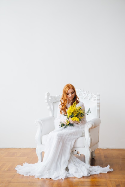 Portrait of a red-haired beautiful girl with a Mimosa in a long white dress