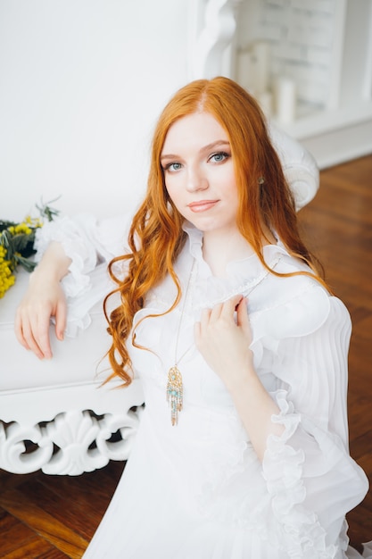 Portrait of a red-haired beautiful girl with a Mimosa in a long white dress