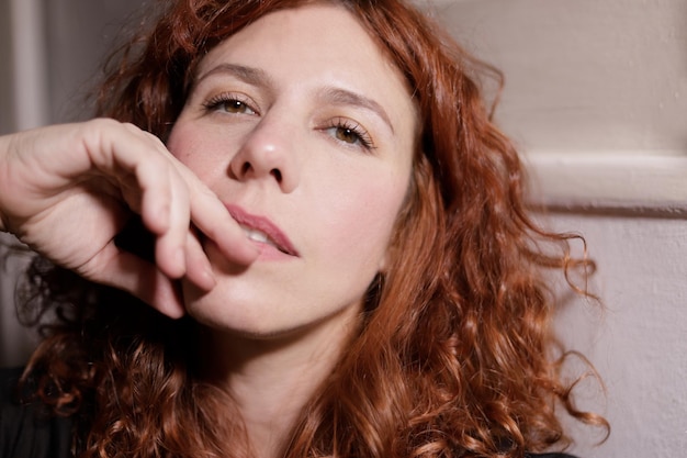 Portrait of red haired woman looking at camera with serene expression and hand next to mouth