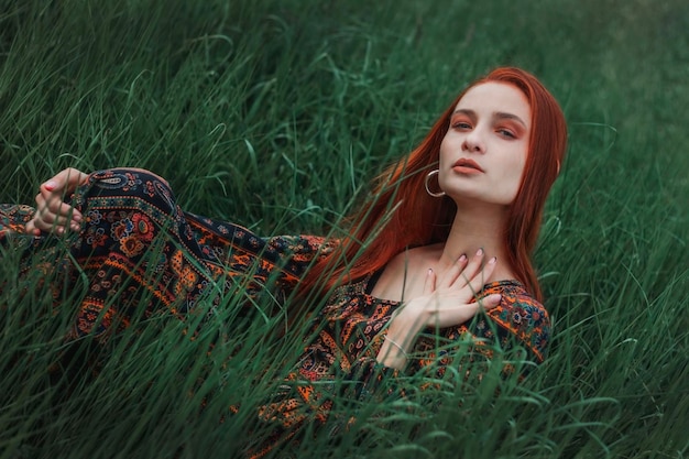 Portrait of a redhaired girl dressed in an ethnic dress Green grass Mountain Merging with nature