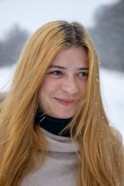 ぼやけた雪の背景を持つ彼女の顔にそばかすのある赤髪の少女の肖像画