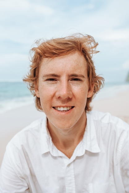 portrait of a redhaired man in white clothes on a white beach