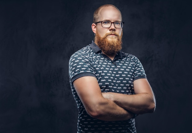 Photo portrait of a redhead bearded male dressed in a t-shirt posing with crossed arms. isolated on a dark textured background.