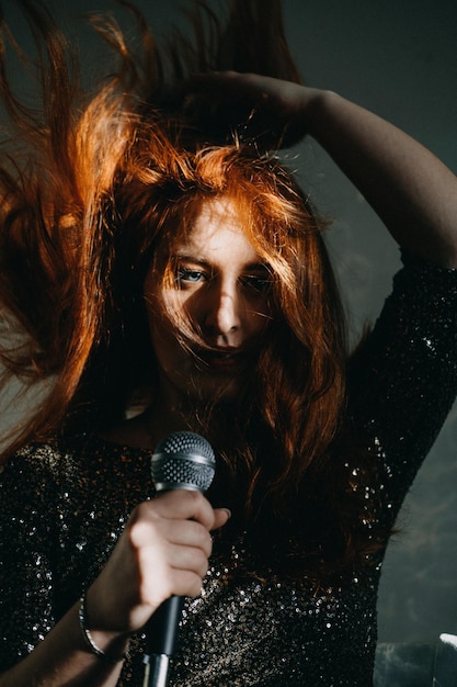 Portrait of redhead female singer woman in sparkly evening dress holding microphone singer at