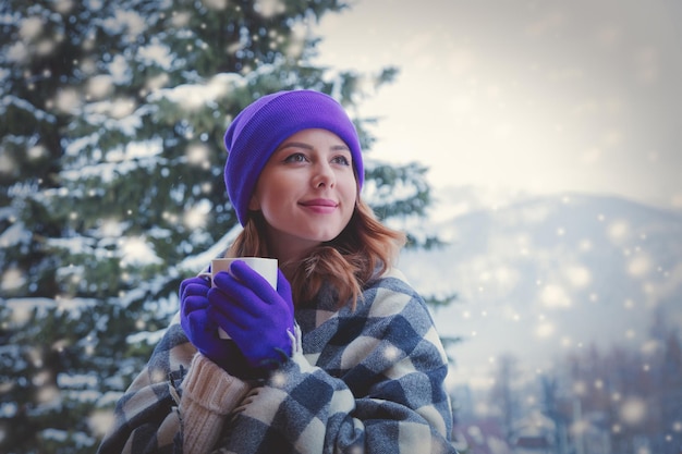 portrait of redhead girl in plaid and purple hat with cup of hot drink at winter outdoor