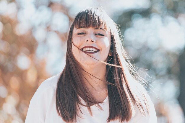 Portrait of redhead young woman walking outside and looking at camera. Happy smiling face. Girl wear white mock up t-shirt. playing with leaf, looking at camera and smiling.